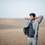 Man standing in field with his hands behind his head