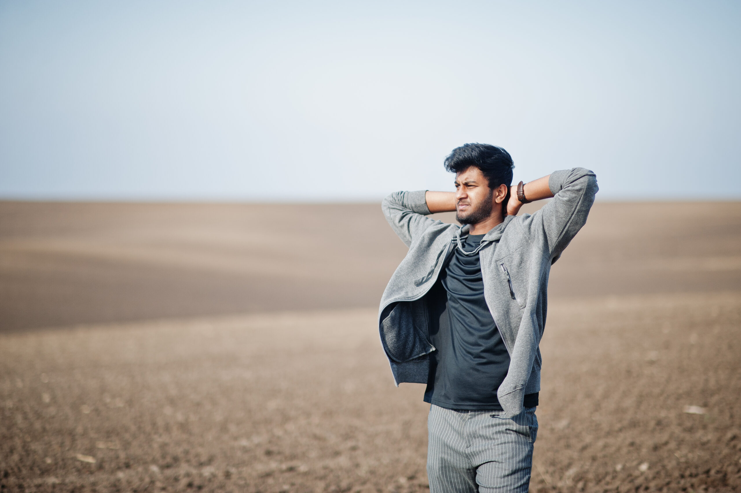 Man standing in field with his hands behind his head