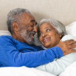 Happy senior biracial couple lying in bed and embracing at home. Senior lifestyle, retirement and domestic life, unaltered.