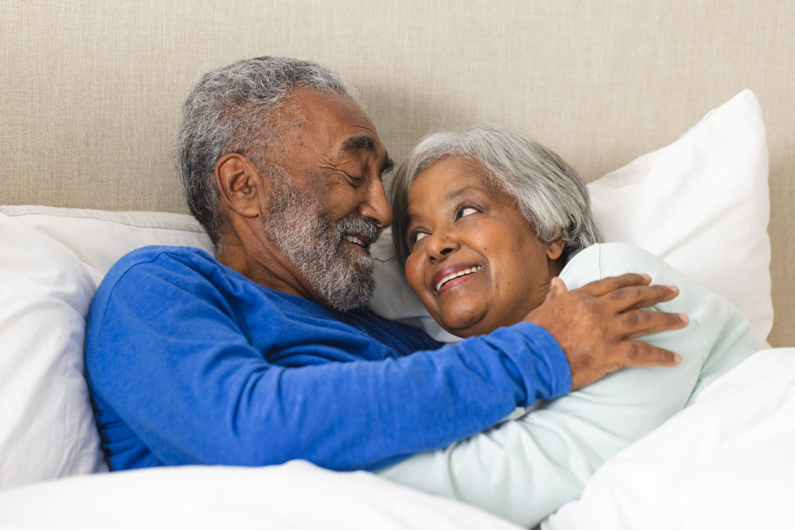 Happy senior biracial couple lying in bed and embracing at home. Senior lifestyle, retirement and domestic life, unaltered.