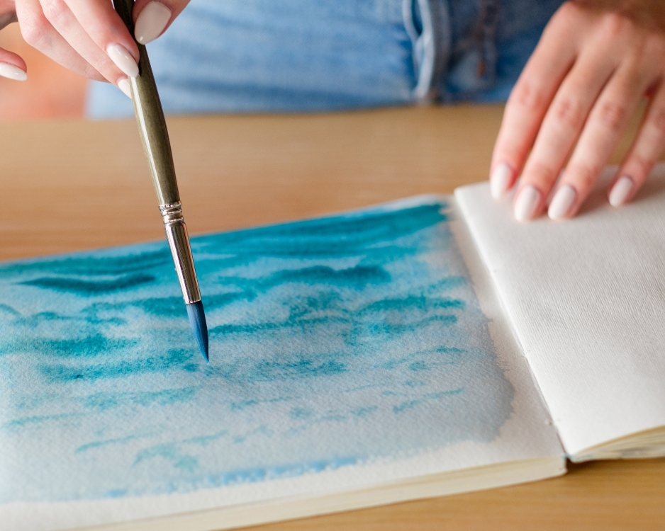 Person painting a page blue using water colors