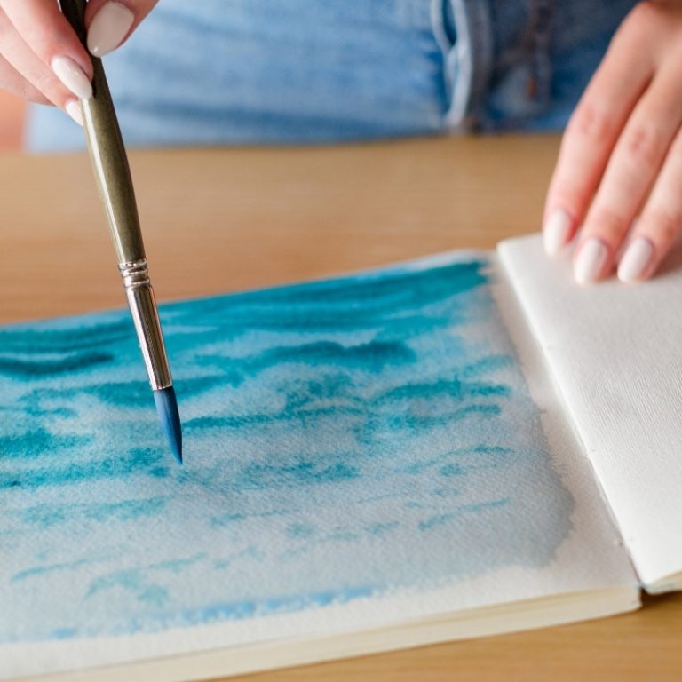Person painting a page blue using water colors