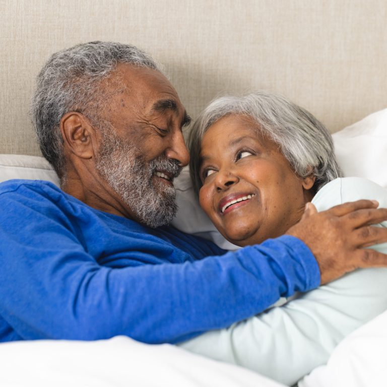 Happy senior biracial couple lying in bed and embracing at home. Senior lifestyle, retirement and domestic life, unaltered.